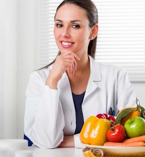 Smiling young Female Dietitian sitting at desk and showing colorful vegetables and fruit, healthy eating and diet concept